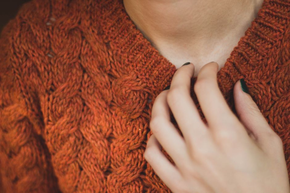A detailed close-up image showcasing a hand touching an orange knit sweater, highlighting fashion and texture.