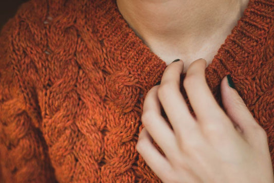 A detailed close-up image showcasing a hand touching an orange knit sweater, highlighting fashion and texture.