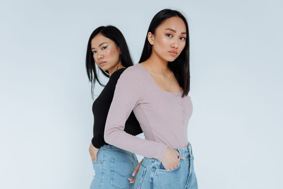 Two Asian women wearing long sleeves, posing confidently in a studio with a white background.